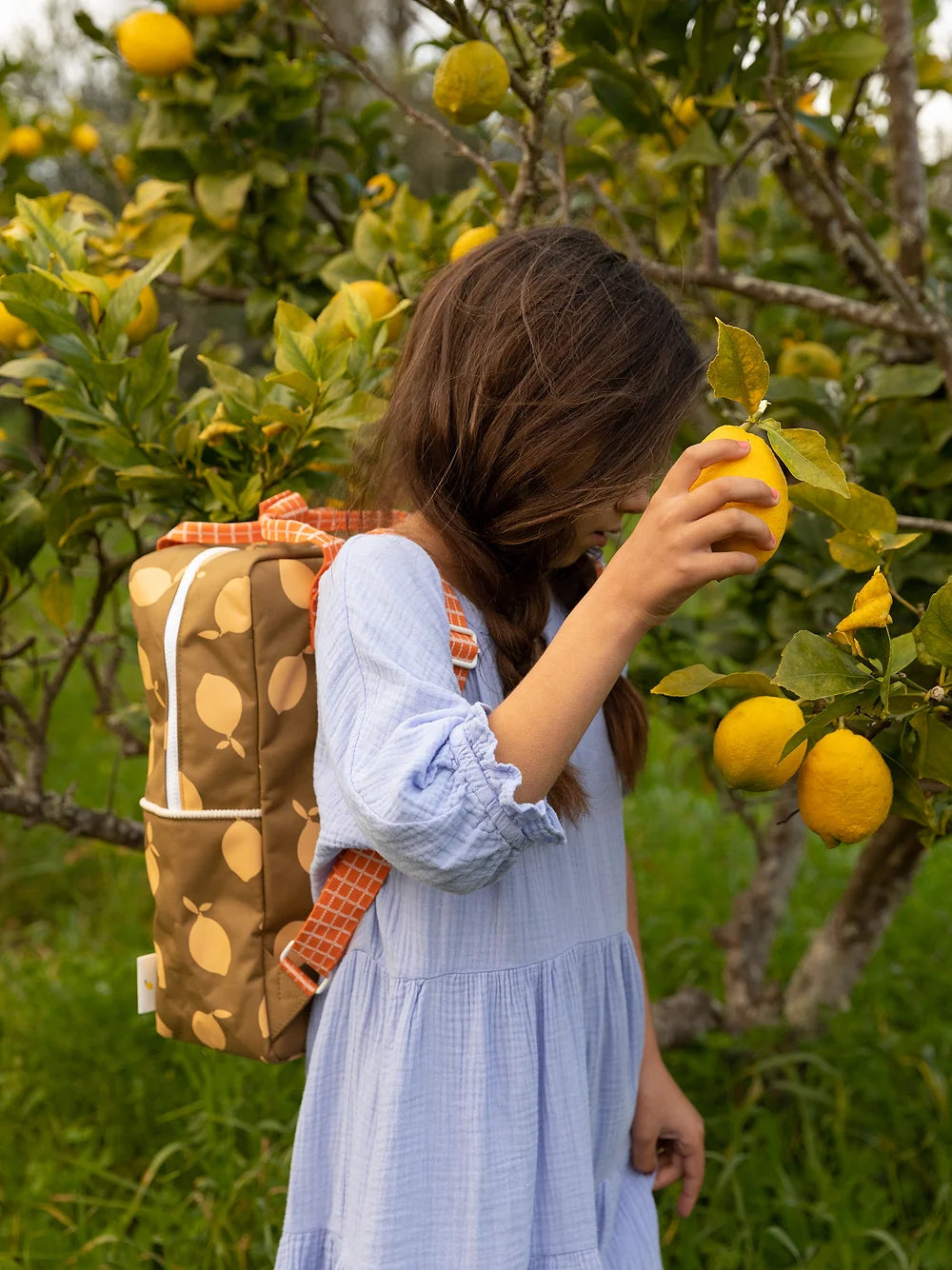 Fille dans un champ de citrons avec Sac à dos brun fait en bouteilles PET recyclées avec citrons oranges partout 