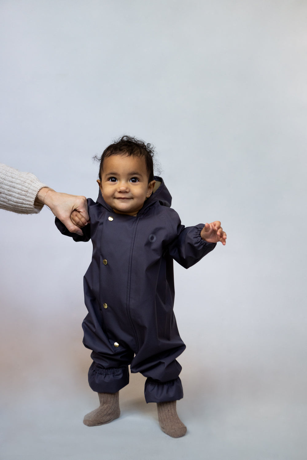 bébé souriant portant la combinaison de pluie Faire Child en indigo. Smiling baby standing up wearing Faire Child's rain onesie in indigo